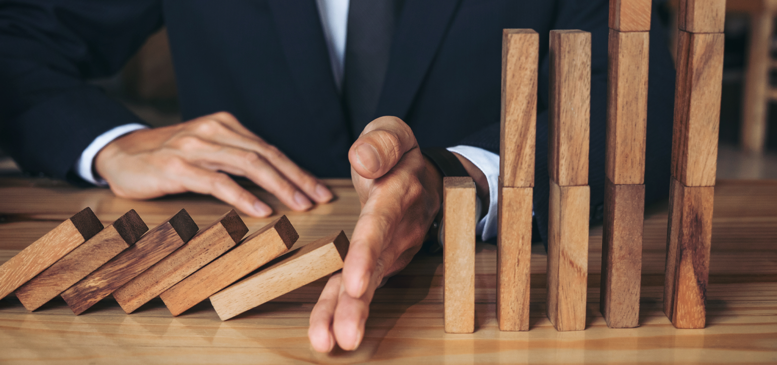 businessman hand stopping falling wooden dominoes