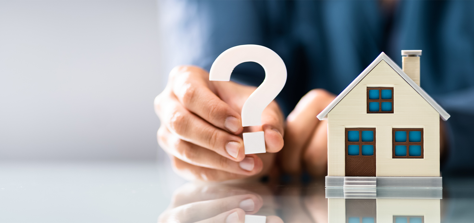 Model house with someone holding a question mark beside it.