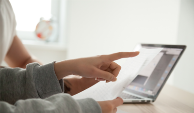 Close up image of two people reviewing a document with a laptop in the background